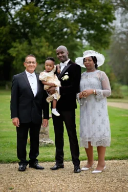 www.thefxworks.co.uk A family dressed in formal attire posing for a photo at Orchardleigh House Weddings, with an older man and woman on the sides, a man holding a baby in the center, and a woman standing