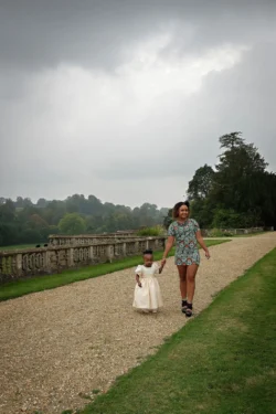 www.thefxworks.co.uk A woman and a young child holding hands while walking on a gravel path beside a stone balustrade at Orchardleigh House, with trees and cloudy skies in the background.