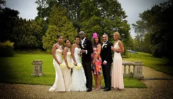 www.thefxworks.co.uk A wedding party posing outdoors at Orchardleigh House with the bride and groom at the center, surrounded by bridesmaids and a flamboyantly dressed officiant.
