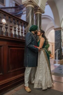 A couple dressed in traditional attire stands closely together in an elegant interior of a guildhall, with arched ceilings and decorative columns.