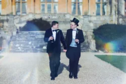 Orchardleigh Wedding Photography captures the elegance of two men in tuxedos walking down a path on their special day.