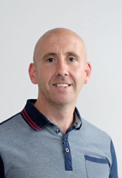 A man with a bald head wearing a short-sleeved, two-toned polo shirt is posing against a plain white background, exemplifying the polished look ideal for corporate photography.