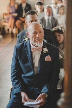 A man in a suit beautifully captured by an Orchardleigh House Wedding Photographer as he sits on the pew during a wedding ceremony.
