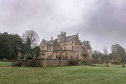 Evoto A large, historic mansion like Orchardleigh House sits amidst a grassy lawn with cloudy skies overhead and surrounding trees, reminiscent of scenes captured in timeless photos.