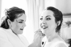 Evoto In a warmly lit room at Orchardleigh House, two women are all smiles, as one in a robe adjusts the other's hair and makeup.