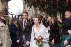 Evoto The bride and groom exit the church, hand in hand and beaming as they're showered with confetti. Guests gather around, some capturing Orchardleigh House photos to cherish the joyous celebration.