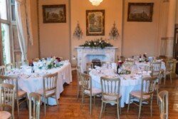 Evoto Elegant dining room with round tables set for a formal event, featuring white tablecloths, floral centerpieces, and a decorative fireplace—a scene reminiscent of Orchardleigh House photos.