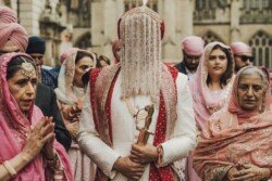 A groom in traditional attire with a beaded headdress holds a ceremonial sword, standing among family members dressed in pink and white during an outdoor ceremony. Capturing these cherished moments is effortless with Fuji Cameras for weddings.