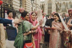 A group of people in traditional attire celebrate outside The Guildhall. A woman in green embraces a bride in pink, surrounded by others in festive clothing, capturing the joyous moment with Fuji Cameras for weddings.