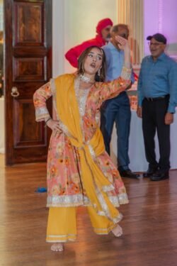 A woman in colorful traditional attire is performing a dance indoors at the Guildhall, while a few people watch in the background.