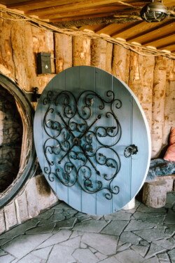 A large, round, blue door with intricate black wrought iron details is set in a rustic stone and wood wall next to a cushioned seating area, perfect for picturesque moments like those at Croftview weddings.