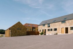 A spacious, paved courtyard is surrounded by modern stone buildings with multiple windows and sloped roofs under a clear blue sky, perfect for picturesque Croftview weddings at Hinton Park.
