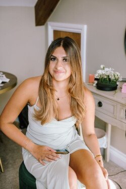 A seated woman in a light green dress holds a phone and smiles at the camera, with a table and plant in the background—another charming moment captured by Croftview Photos.