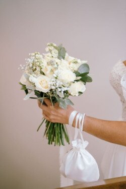 A bride holds a bouquet of white roses and baby's breath, along with a small white satin bag. Captured beautifully by Croftview Photos, each detail exudes elegance.