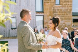 A couple exchanges vows during an outdoor wedding ceremony captured by Croftview Photos. The bride holds a bouquet and smiles at the groom, while guests are seated and watching in the background.