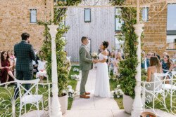 A couple stands under a decorated arch exchanging vows during an outdoor wedding ceremony; guests are seated on both sides, moments beautifully captured by Croftview Photos.