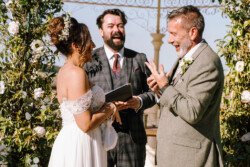 A couple exchanges vows and laughs during an outdoor wedding ceremony, with an officiant standing behind them. This magical moment was beautifully captured by Croftview Photos.