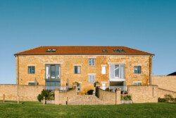 A large two-story brick building with a red-tiled roof, multiple windows, and a central entrance stands proudly at Hinton Park Estate. The front features a staircase flanked by short walls, leading to green lawns and a clear blue sky—an ideal setting for Croftview Weddings.