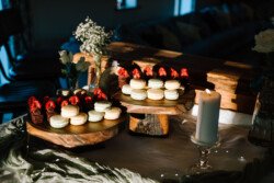 Two wooden stands hold white macarons topped with strawberries and chocolate-dipped strawberries on a table with a lit candle and flower vases, perfect for a Croftview Weddings celebration at Hinton Park Estate.