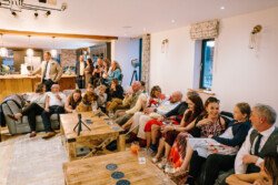 A group of people gathered in a room, some sitting on couches and others standing. The room at Croftview Weddings in Hinton Park Estate is well-lit with modern decor, a wooden counter, and various refreshments on the table.