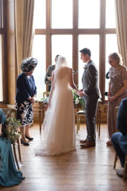 Orchardleigh Wedding Photographer captures an enchanting ceremony as a bride and groom exchange heartfelt vows in a large room.