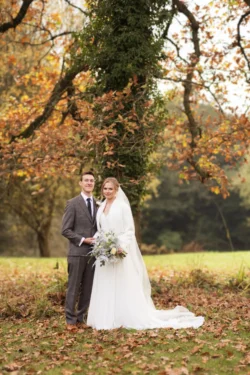 A bride and groom standing in a field with autumn leaves captured by Orchardleigh Wedding Photographer.