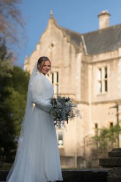 A bride in a white dress standing in front of a large building captured by the Orchardleigh Wedding Photographer.