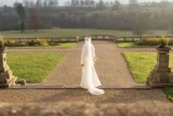 Orchardleigh Wedding Photographer captures a bride gracefully walking down a path in the beautiful garden.