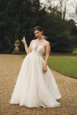 A bride in a white dress posing with a playful gesture on a gravel path at Orchardleigh House Weddings.
