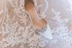 A single white bridal shoe with jewel embellishments, placed on a lace-patterned fabric at Orchardleigh House Weddings.