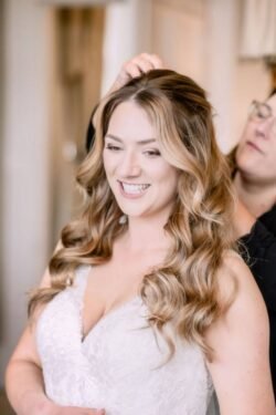 A woman in a white dress smiling as another person adjusts her hair in a well-lit room at Orchardleigh House.