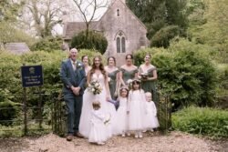 A group of seven people, including adults and children in formal attire, posing in front of Orchardleigh House surrounded by greenery.