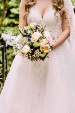 Bride in a white dress holding a bouquet of various flowers at Orchardleigh House, focusing on the upper part of her gown and the bouquet.