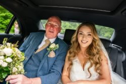 A bride and her father smile inside a car at Orchardleigh House Weddings, the bride holding a bouquet, both dressed in wedding attire.