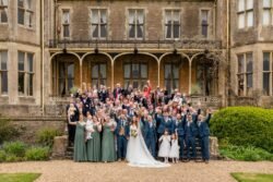 A large wedding party posing in front of the elegant Orchardleigh House with celebratory expressions.