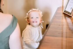 Toddler girl with flower headband smiling beside adult at an Orchardleigh House Weddings cafe table.