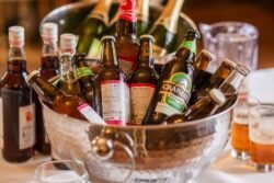 A variety of beers and cider bottles chilled in a metal bucket on a table at Orchardleigh House Weddings, with a glass of beer in the background.