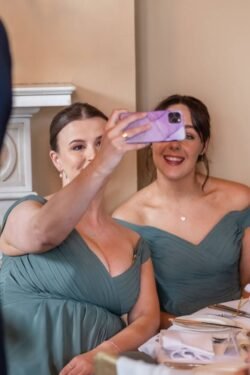 Two women in green dresses taking a selfie at Orchardleigh House Weddings, smiling joyfully, seated at a dining table.