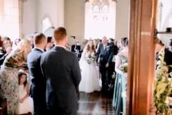 Bride and groom smiling at each other as they meet at the aisle, surrounded by guests at an Orchardleigh House wedding ceremony.