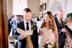 Bride and groom reading from papers during an Orchardleigh House wedding ceremony, with guests seated in the background.