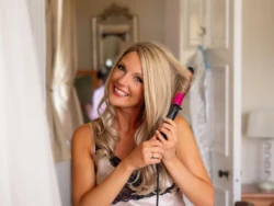 OLYMPUS DIGITAL CAMERA A woman smiling while using a hairdryer and being captured by a world-class wedding photographer.