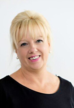 A blonde woman with a smile, wearing a black top with an off-white background, perfect for corporate photography & video services.