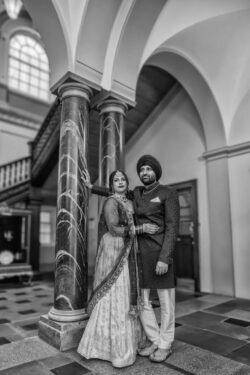 A couple dressed in traditional attire stands in an ornate building with large pillars and arched ceilings, captured beautifully by a wedding photographer at Guildhall Bath.