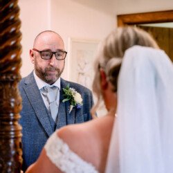 A man in a suit and glasses gazes thoughtfully at a woman in a wedding dress and veil, their reflection captured as if by an Elmhay Park Wedding Photographer.