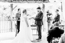 At Elmhay Park, the wedding photographer captured a couple exchanging rings under a wooden gazebo, with the officiant and guests witnessing their vows.
