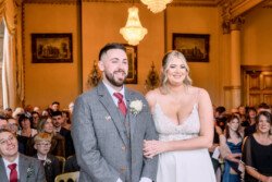 Evoto A couple stands at the altar during a wedding ceremony in an ornate room at Orchardleigh House, surrounded by guests.