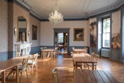 Elegant dining room with wooden tables, chairs, and a chandelier. Large windows allow natural light. Perfect for capturing timeless moments, this space is ideal for a Hartham Park wedding photographer seeking classic charm with ornate ceiling and wall details enhancing the atmosphere.
