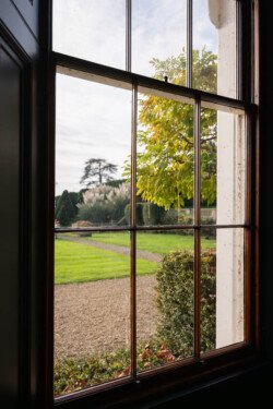 View through a window reveals a picturesque garden with a gravel path, manicured lawn, and trees under a cloudy sky—perfect for capturing enchanting memories with the eye of a Hartham Park wedding photographer.