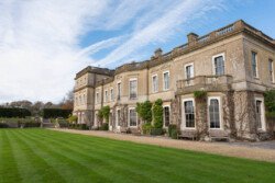 The historic mansion, with its ivy-covered walls and large windows, stands elegantly under a blue sky. Perfect for capturing timeless moments, the manicured lawn offers an enchanting backdrop that any Hartham Park wedding photographer would cherish.