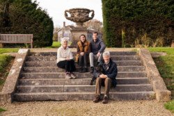 Four people and a dog sit on the stone steps of a garden at Hartham Park, with a large urn and towering trees framing the perfect wedding photographer's backdrop.